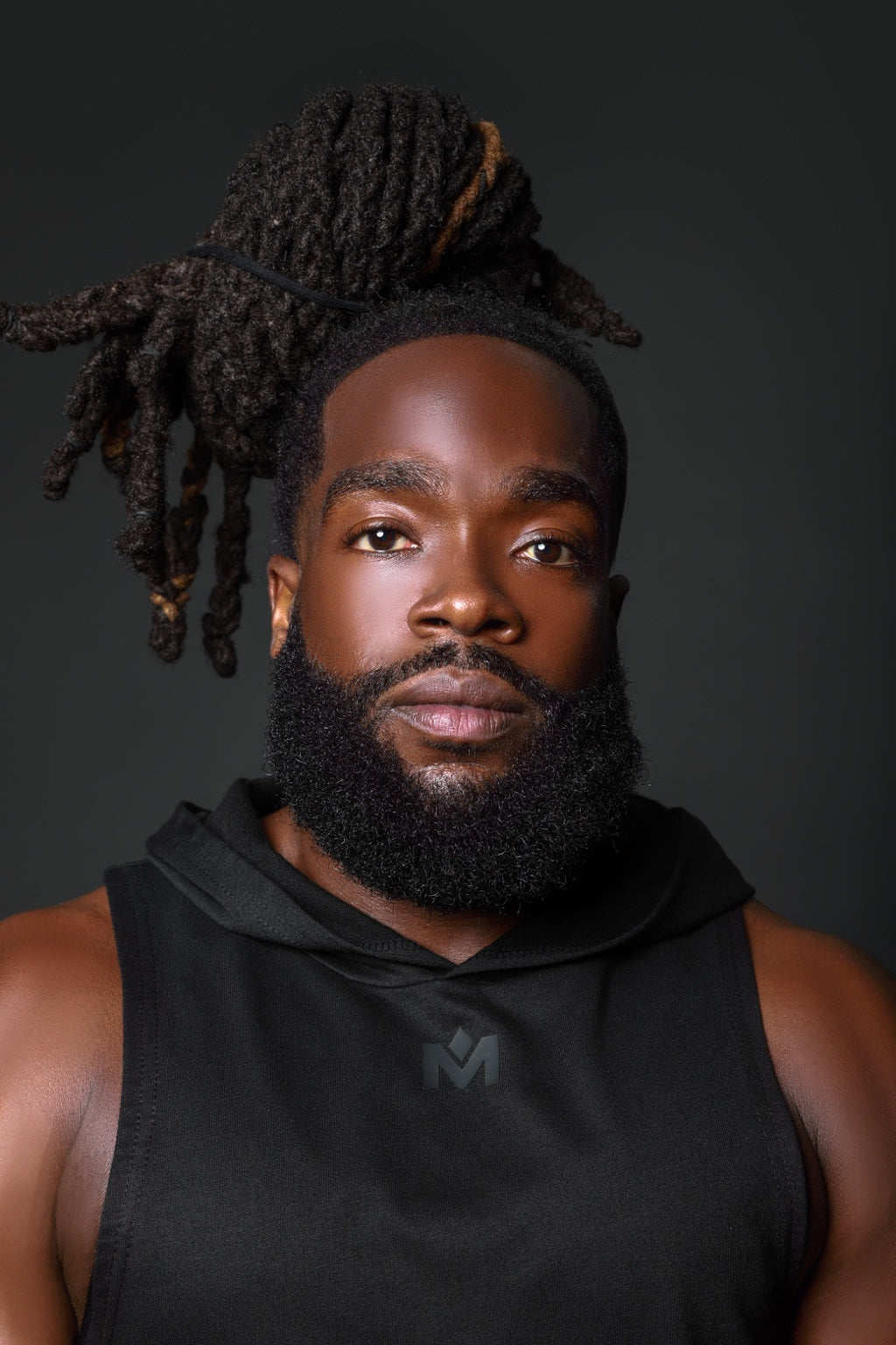 Close-up portrait of a model wearing the black Quiet Hood™ sleeveless performance hoodie with tonal Mogul M logo